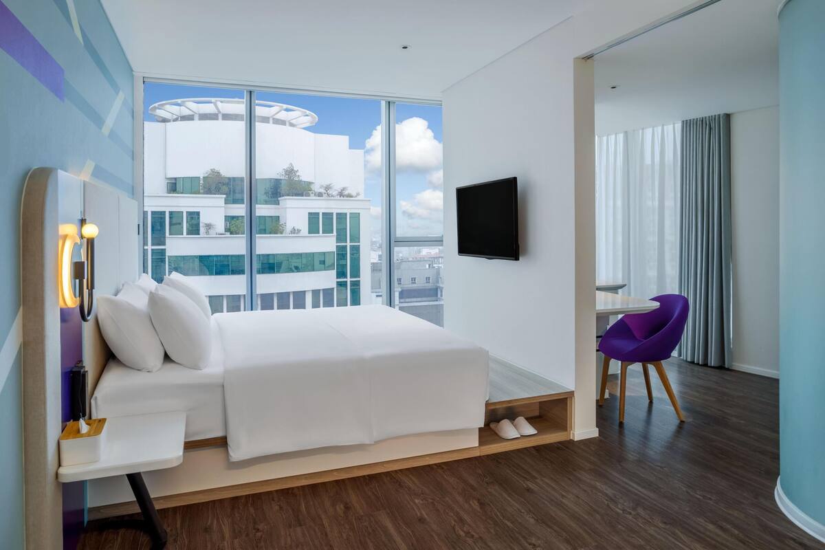 A modern hotel room with a large bed, a desk, a chair, and a TV.