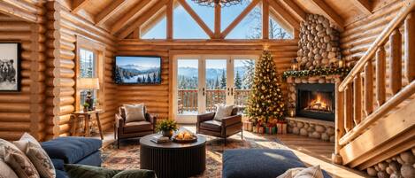 A log cabin interior with a fireplace, a Christmas tree, and a cozy seating area.