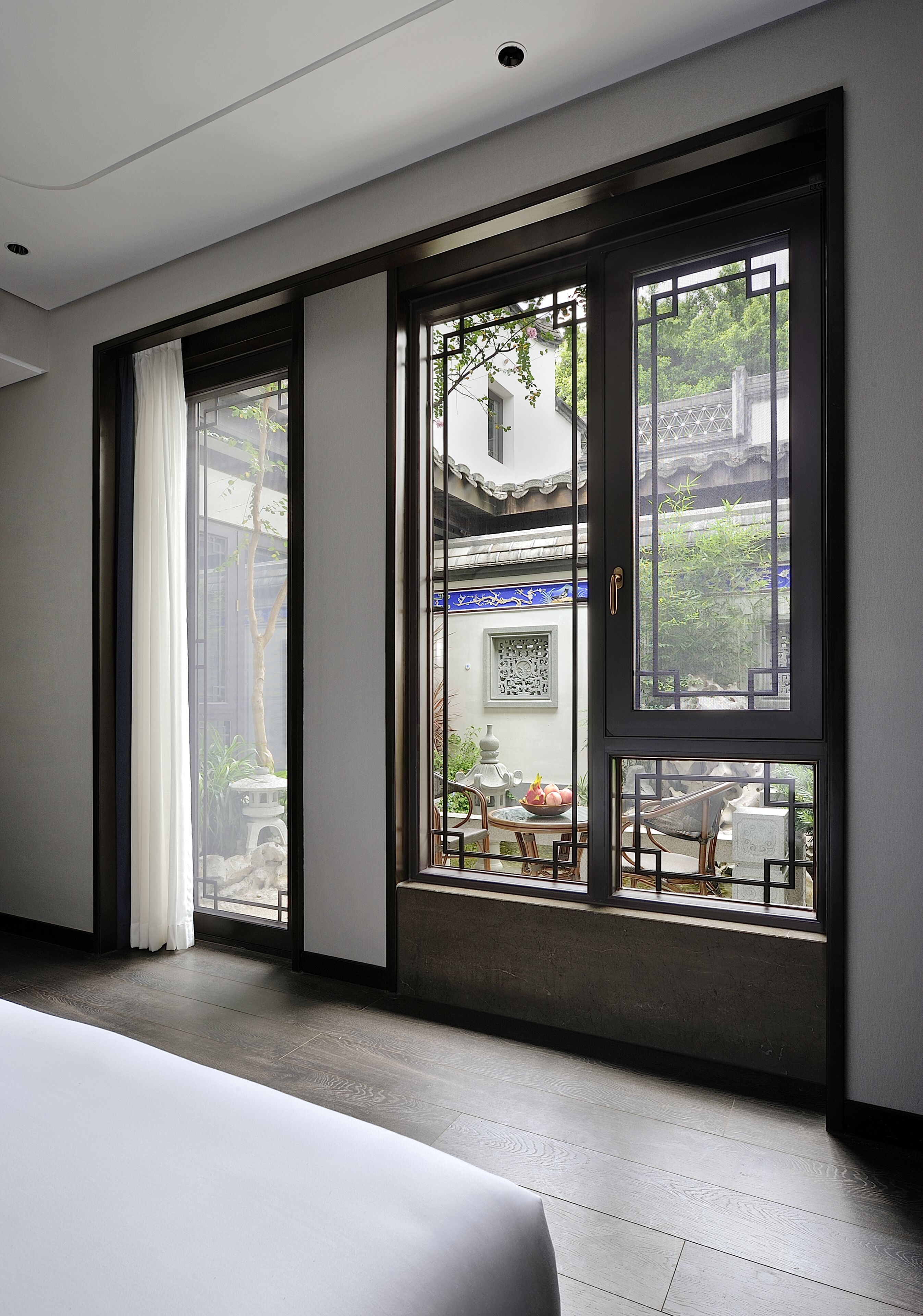 A modern hotel room with large windows, a bed, and a view of the courtyard.