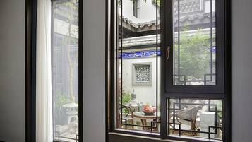 A modern hotel room with large windows, a bed, and a view of the courtyard.