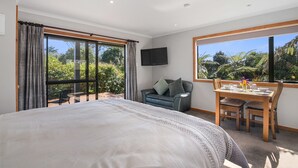 A bedroom with a large bed, a TV, a balcony with a sofa, and a dining area with a table and chairs.