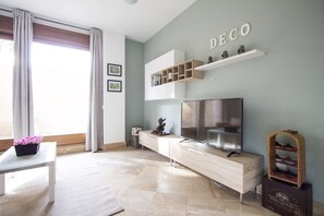 A modern living room with a TV, wooden cabinet, and a 'DECO' sign on the wall.