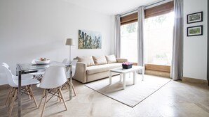 Ein modernes Wohnzimmer mit einem Glastisch, weißen Stühlen, einem beigen Sofa und einem Couchtisch.