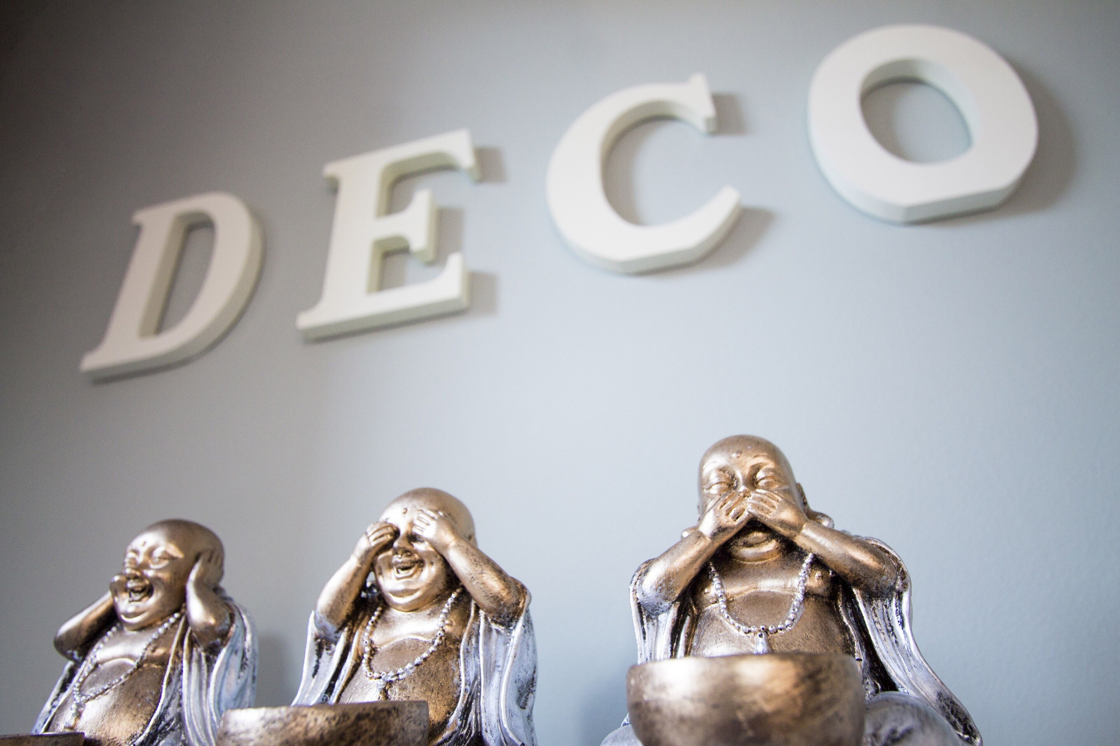 Una pared con las letras "DECO" y tres estatuas de Buda sonriendo.