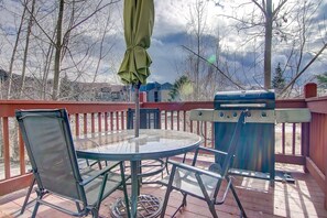 Una terraza con una mesa redonda de vidrio, sillas de metal, una parrilla y un paraguas verde.