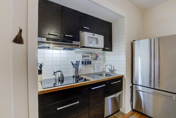 A modern kitchen with dark cabinets, a stainless steel refrigerator, a microwave, and a sink. - Cute Cottage, Walk to Overton Park & Memphis Zoo (Memphis)