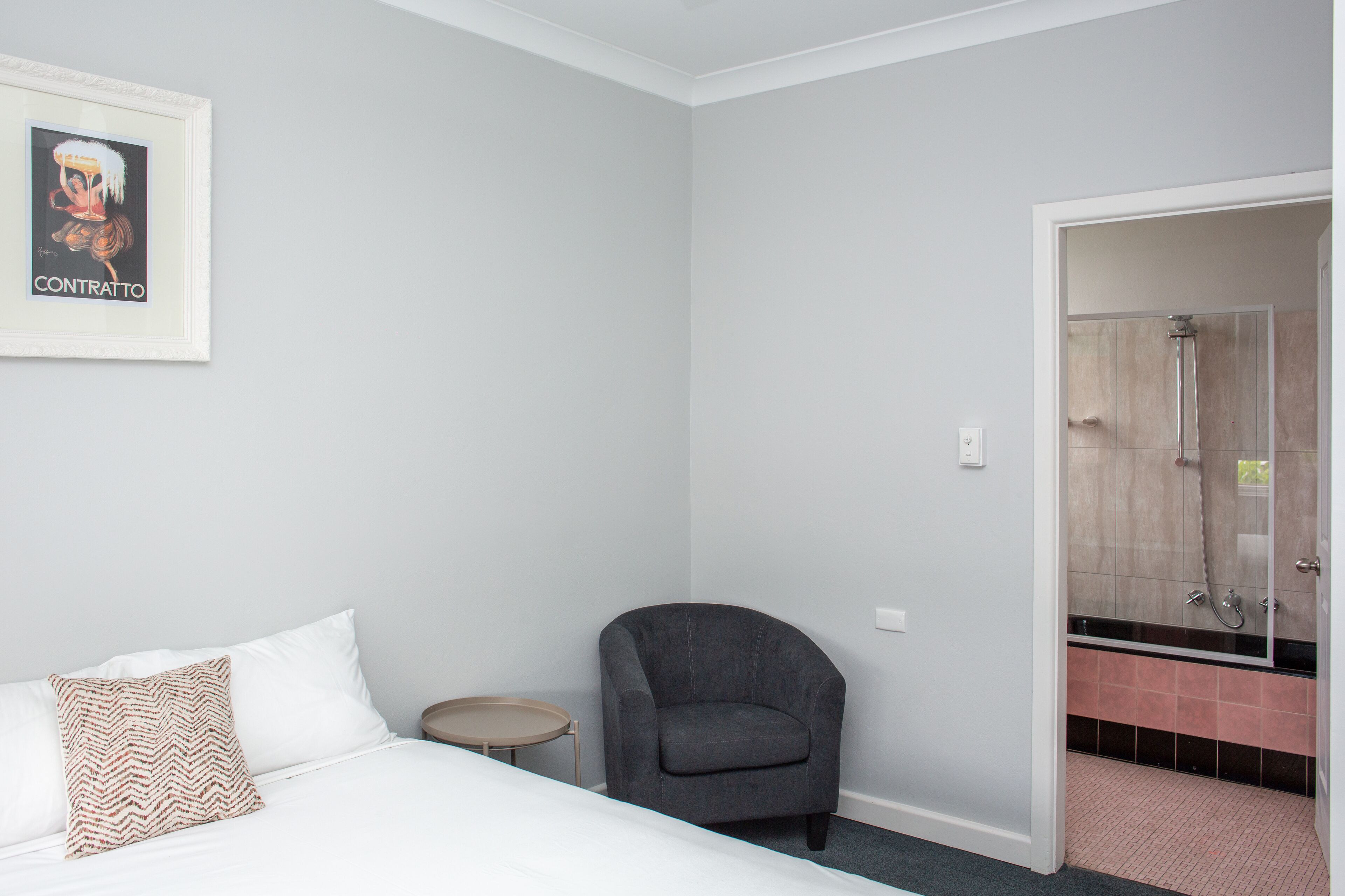 Een hotelkamer met een bed, een stoel, een tafeltje en een badkamer zichtbaar door een geopende deur.