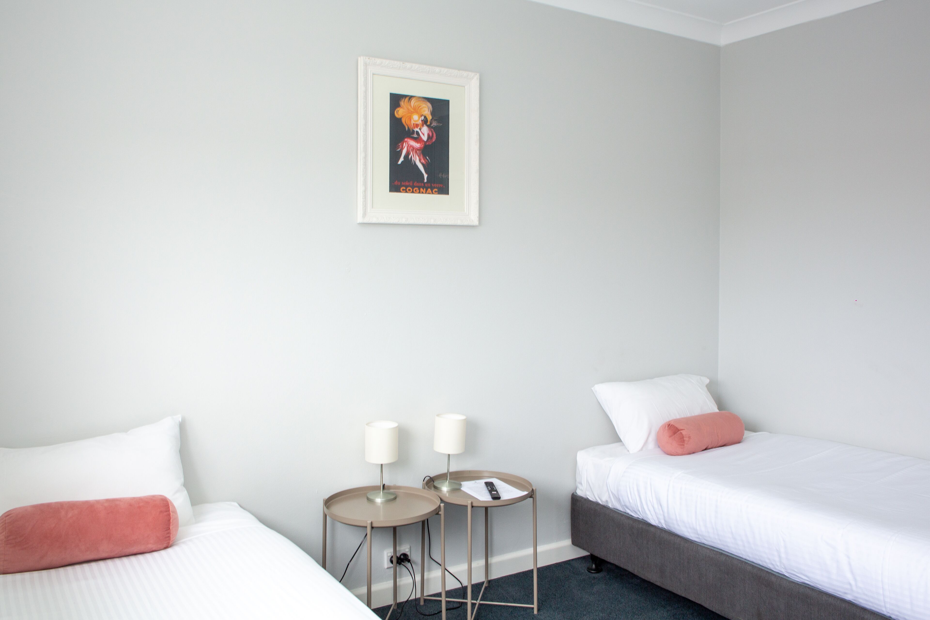 Una habitación de hotel con dos camas, una mesita con lámparas y un cuadro enmarcado en la pared.