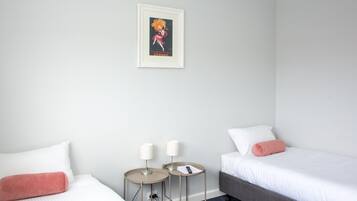 Una habitación de hotel con dos camas, una mesita con lámparas y un cuadro enmarcado en la pared.