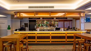 Zona de bar con taburetes de madera, una barra con exhibición de botellas y un cartel que indica un espacio para eventos deportivos.