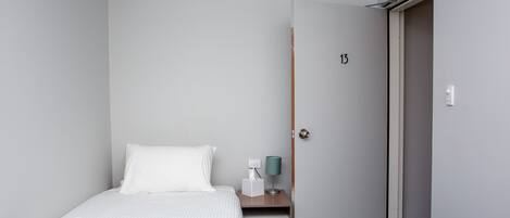 Quarto de hotel com uma cama, mesa de cabeceira com abajur, porta com o número 13 e um pequeno degrau que leva a um armário.