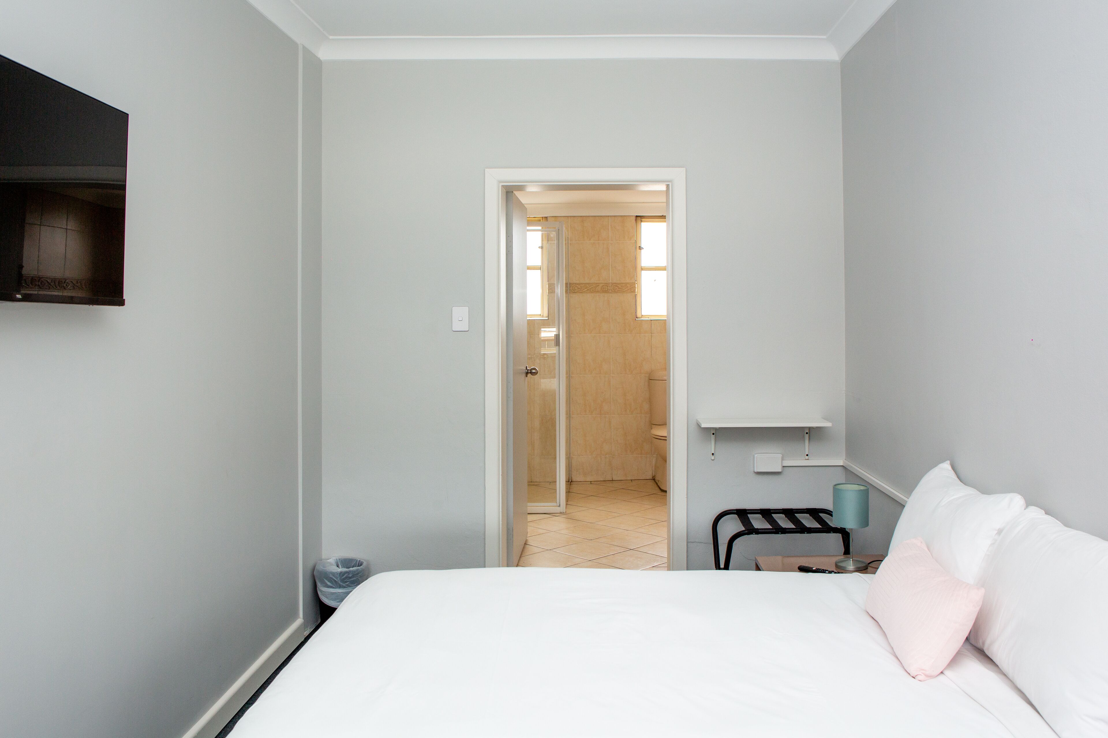 Une chambre à coucher comprenant un lit, une table de chevet, une lampe et une porte donnant sur une salle de bain.