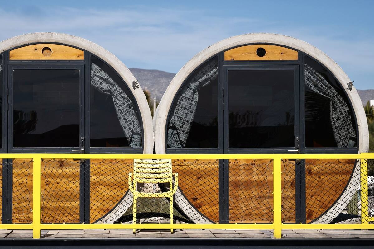Dos estructuras grandes y semicirculares con puertas negras y ventanas de malla, rodeadas por una valla amarilla.