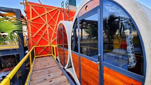 A modern, cylindrical structure with large windows and a wooden deck. - ChangoMango (La Ventana)