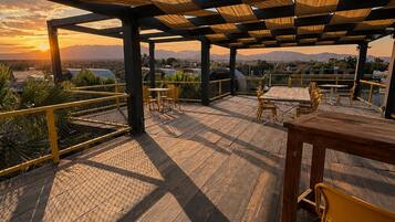 An outdoor patio with wooden flooring and tables, overlooking a mountainous landscape.