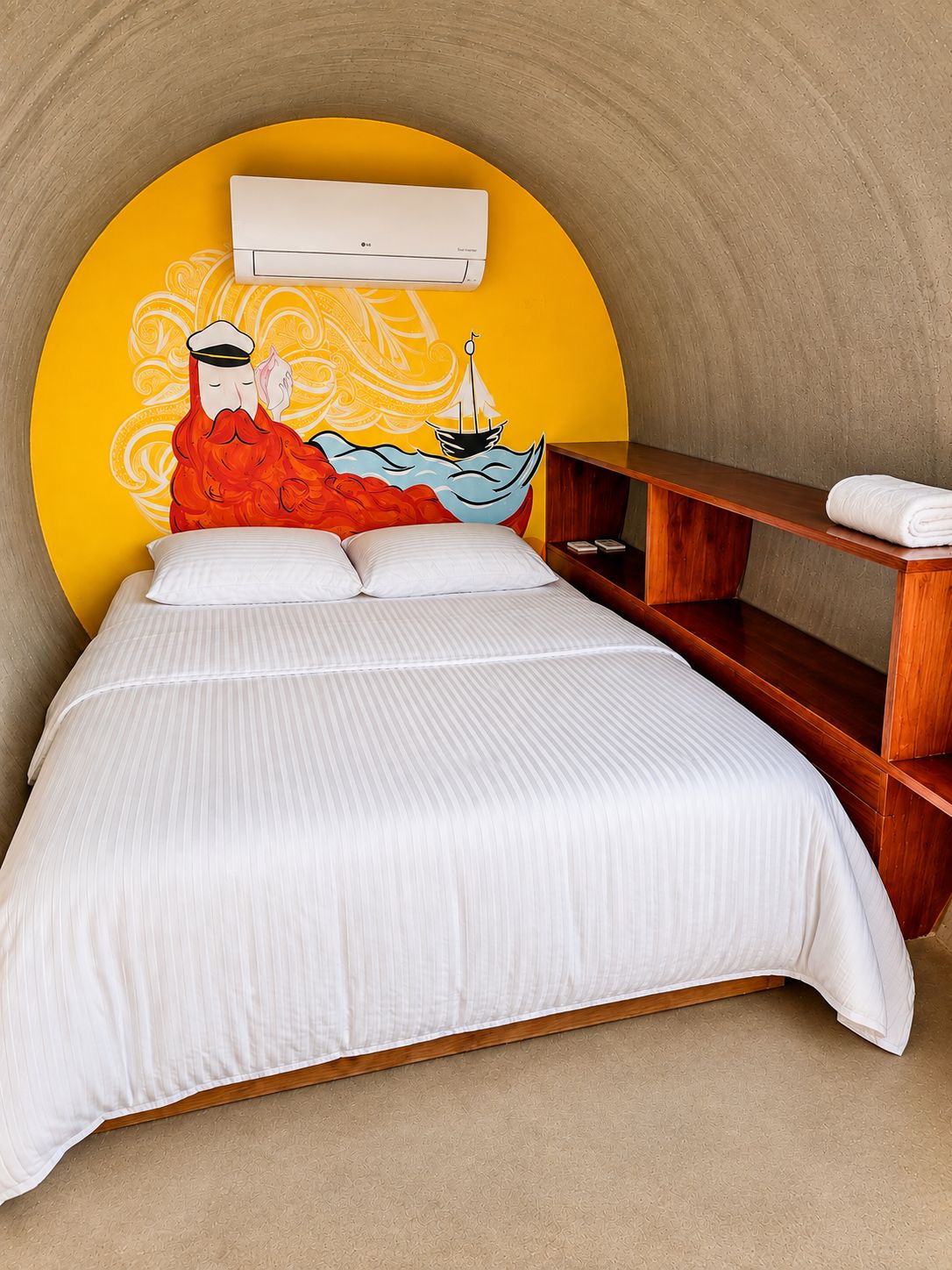 A bed with a white striped bedspread, a wooden nightstand, and a wall-mounted air conditioning unit.