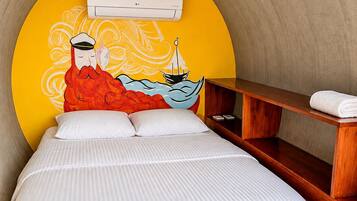 A bed with a white striped bedspread, a wooden nightstand, and a wall-mounted air conditioning unit.
