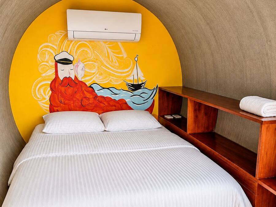 A bed with a white striped bedspread, a wooden nightstand, and a wall-mounted air conditioning unit.