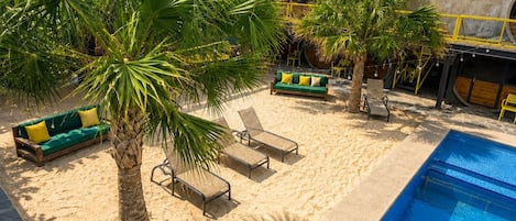 A pool area with lounge chairs, a palm tree, and a building with a sign.