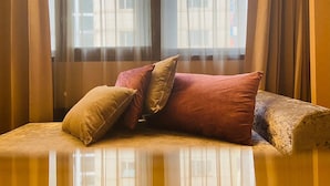 A sofa with cushions in a room with sheer curtains and a view of buildings outside. - Artinn hotel (Taipei)