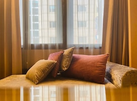Un sofá con cojines en una habitación con cortinas translúcidas y vistas a edificios.