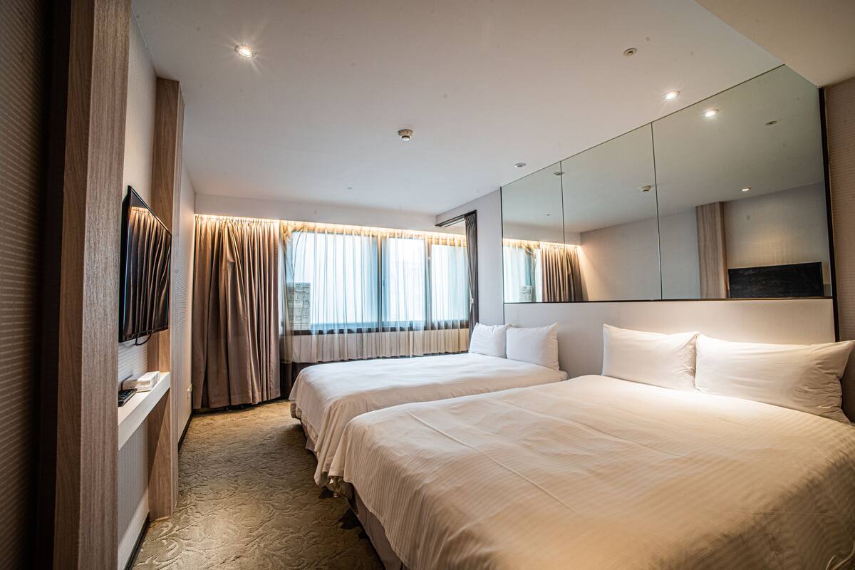A hotel room with two beds, a large mirror, and a television on a stand.