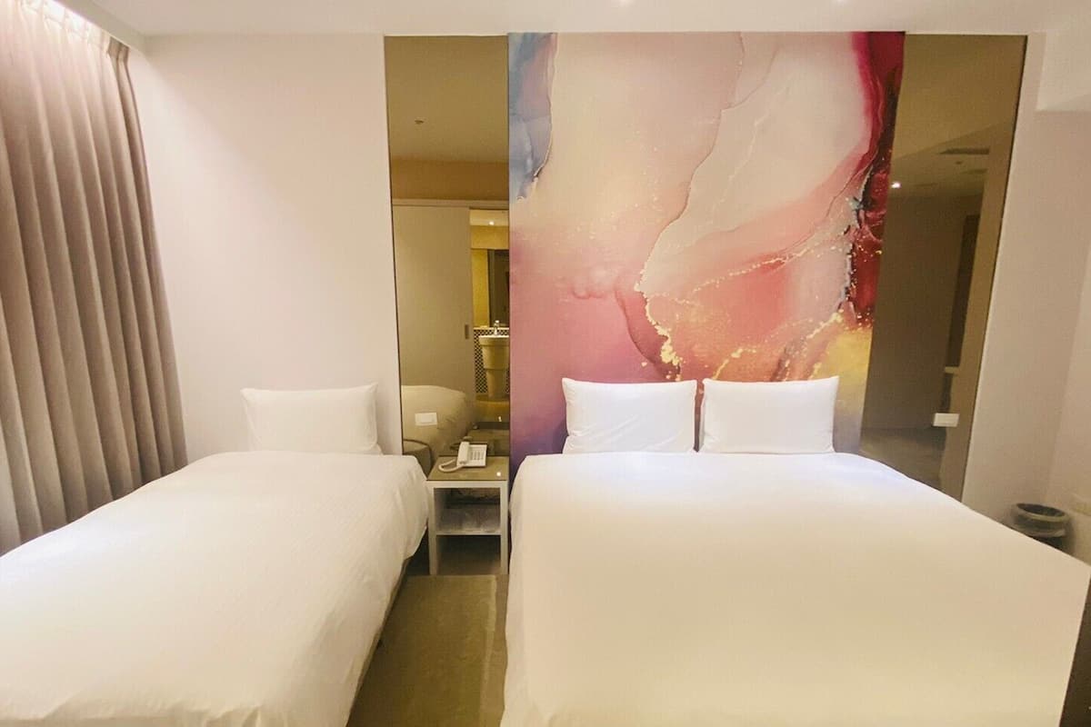 A hotel room with two single beds, a bedside table with a phone, and a large abstract painting on the wall.