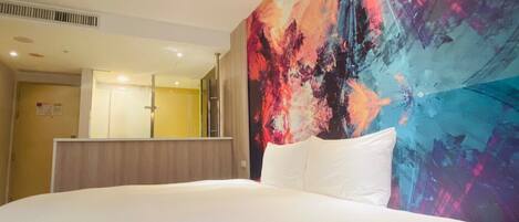 Una habitación de hotel con una cama grande, un mural abstracto de colores y un espejo.