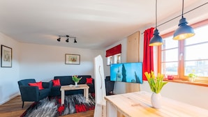 A modern living room with a dark blue sofa, red cushions, a wooden coffee table, and a flat-screen TV. - Vacation apartment "Jakobo" 44sqm, balcony (Eggstätt)