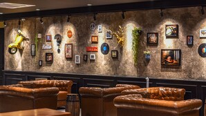 A lobby with leather sofas, a wooden table, and a wall decorated with various framed items and a yellow scooter. - Zone Hotel Ipoh (Ipoh)