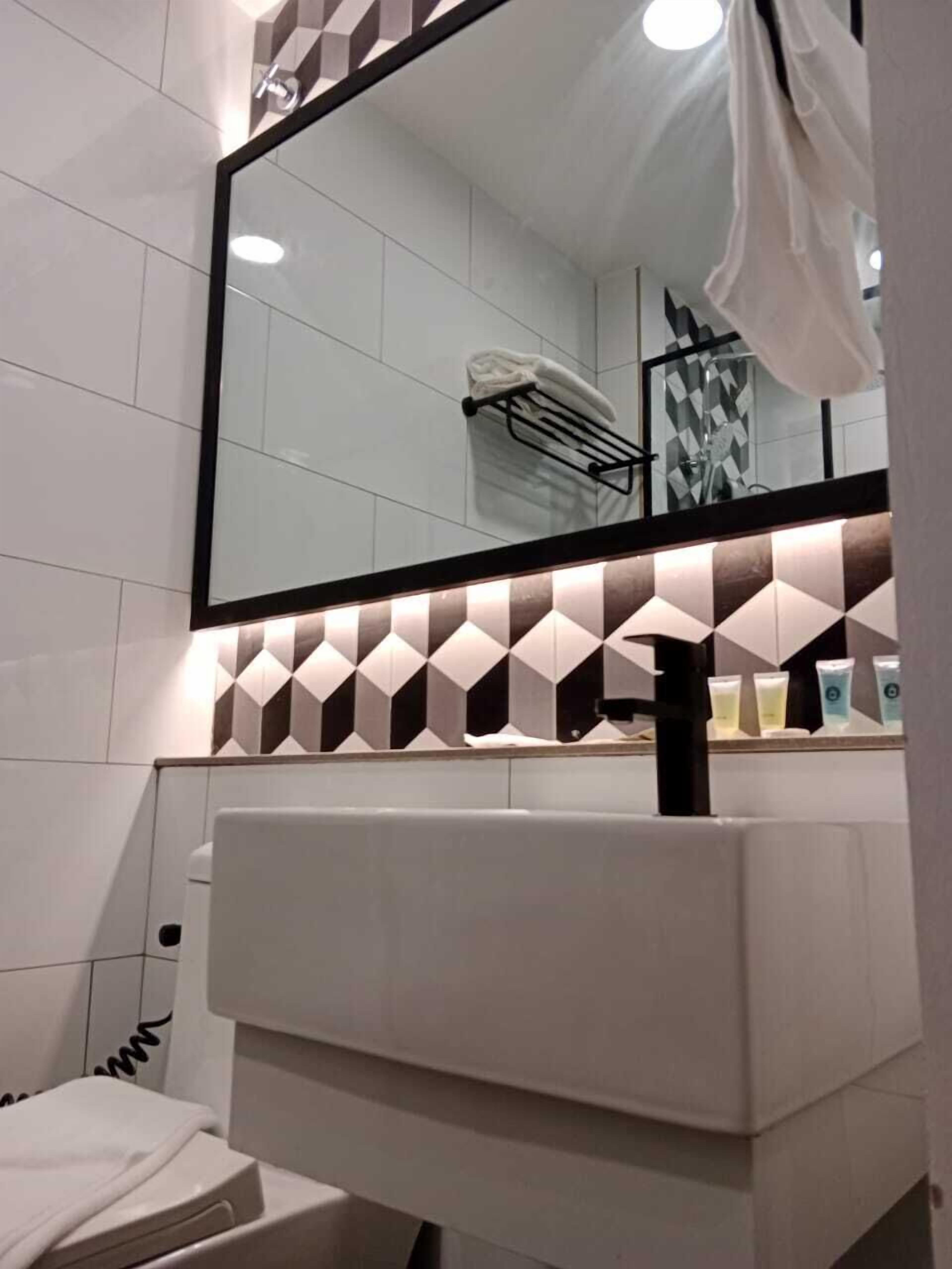 A modern bathroom with a large mirror, a white sink, and a geometric patterned wall.