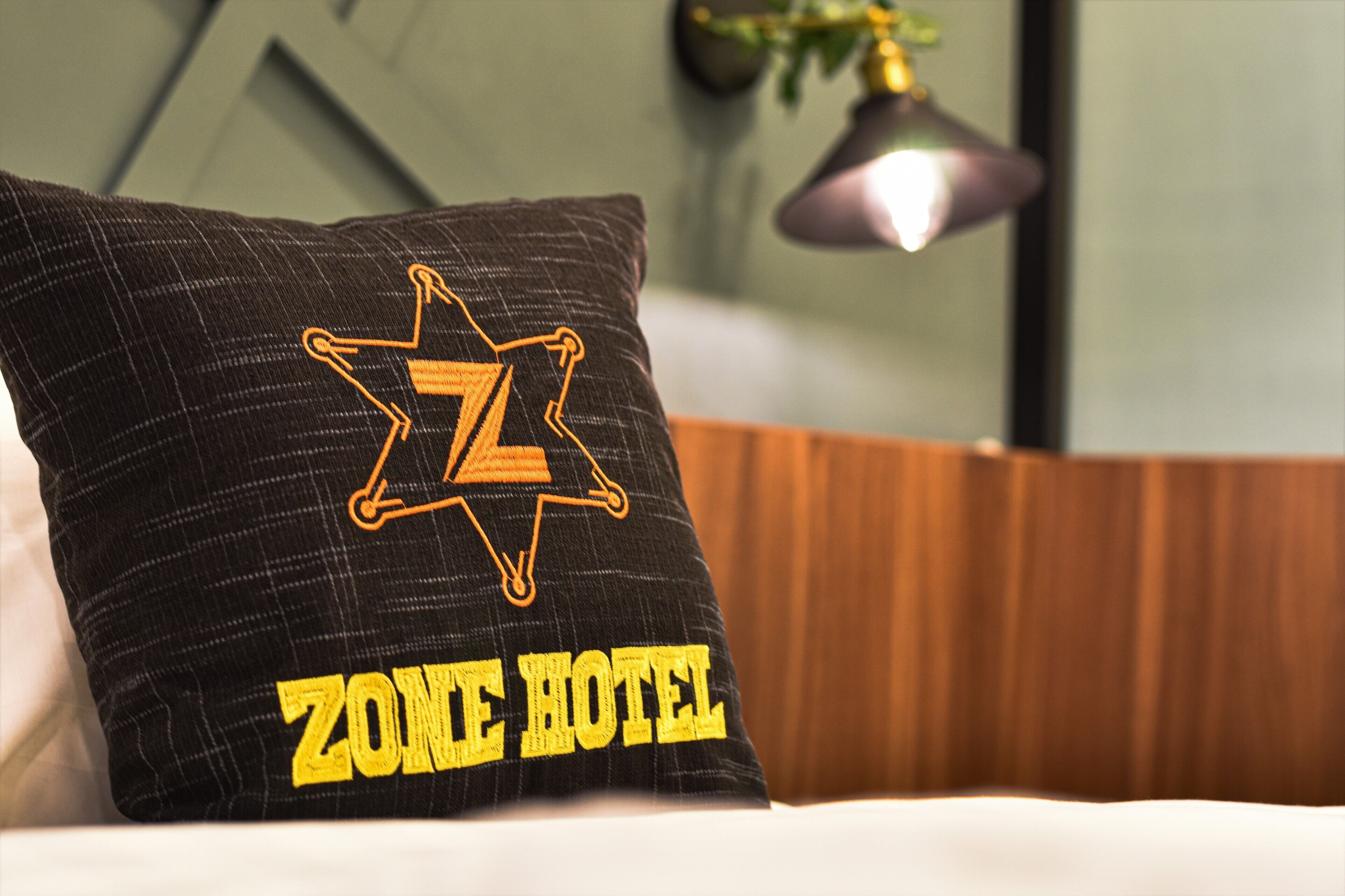 A black pillow with a yellow embroidered star and the words "ZONE HOTEL" on a bed.