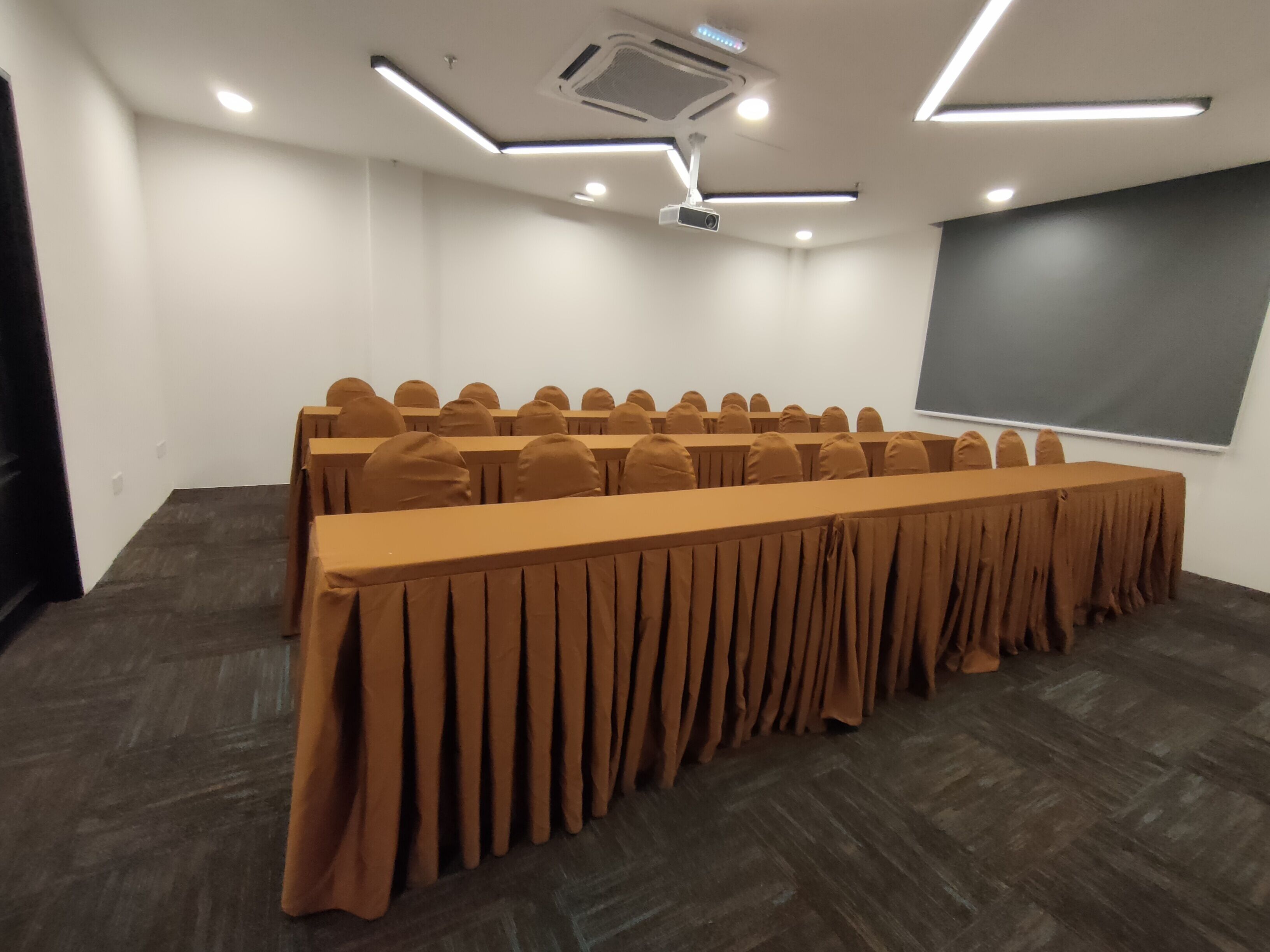 A conference room with a long table, rows of chairs, a projector, and a screen.