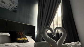 A hotel room with a bed, a pillow with a logo, a window with curtains, and a swan-shaped towel arrangement.