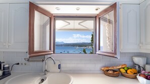 Una cocina con vista al mar por la ventana, un fregadero y fruteros sobre la encimera.