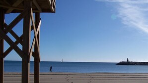 A beach with a wooden structure, a person standing, and a lighthouse in the distance.