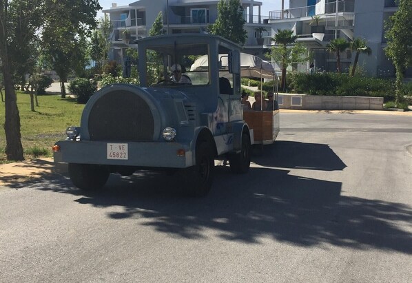 Een oudere auto met een nummerplaat, geparkeerd op een straat met gebouwen en bomen op de achtergrond.