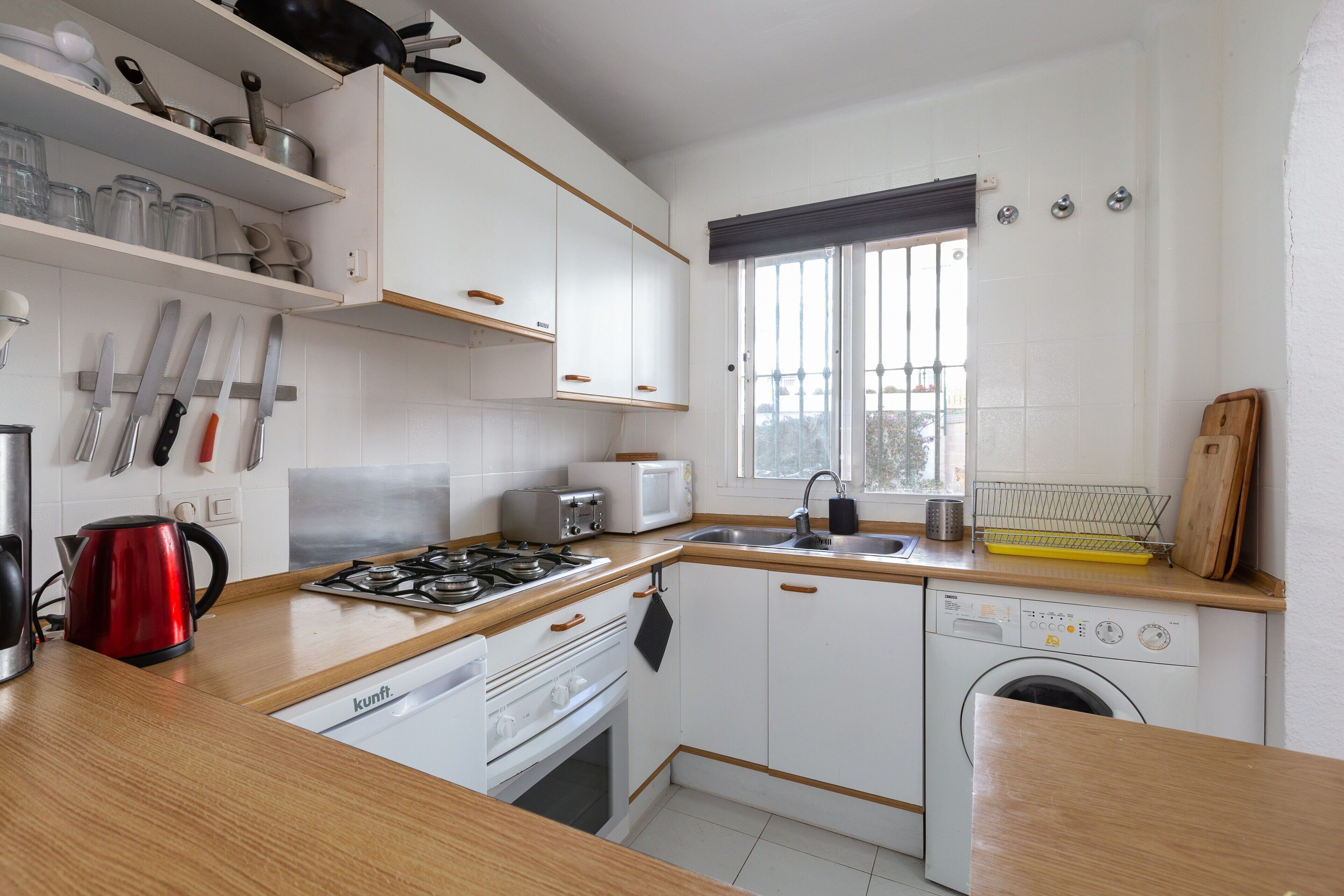 A compact kitchen with white cabinets, a stove, a microwave, and a dishwasher.