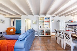 A living room with a sofa, a dining table with chairs, a cabinet with dishes, and a blue door.
