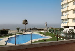 Una piscina con vista al mar, una palmera y un edificio con balcones.