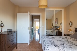 Een slaapkamer met een bed, een kast, een spiegel en een deur naar een andere kamer.