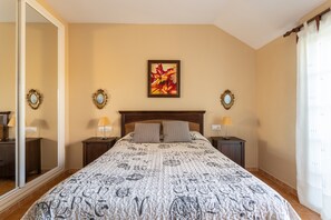 Un dormitorio con una cama grande, dos mesitas de noche con lámparas, un espejo y un cuadro colgado en la pared.