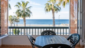 Un balcón con mesa y sillas, con vista a una playa de palmeras y mar.
