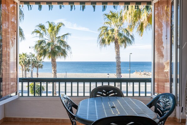 A balcony with a table and chairs, overlooking a beach with palm trees and the sea. - Vacation Apartment "Beautiful Duplex in Salobreña" with Sea View, Pool, Wi-Fi & Terrace (Salobreña)