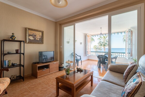 Een woonkamer met een bank, salontafel, televisie, boekenkast en een balkon met tuinmeubilair.