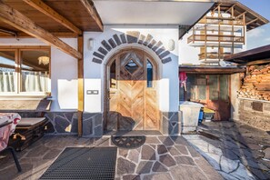 Une entrée dallée de pierre avec une porte en bois, un balcon et un mur de pierre agrémenté d’une cheminée.