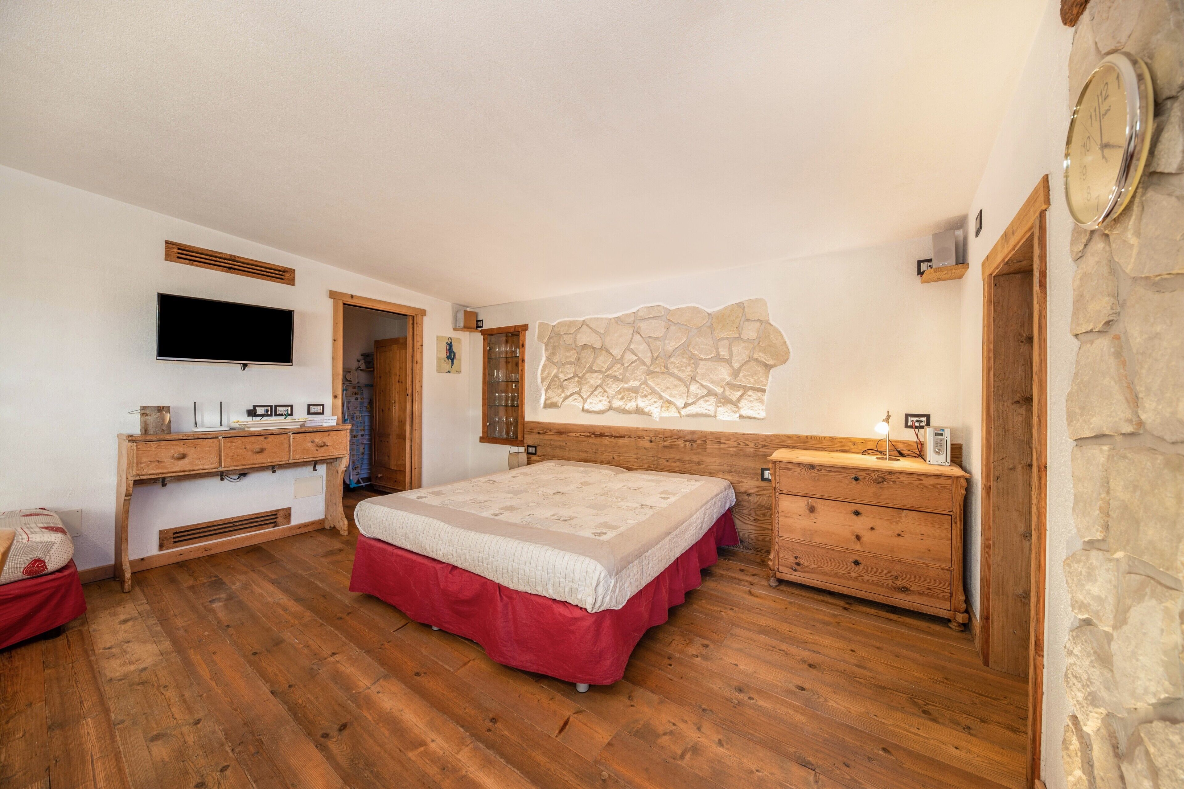 Ein Schlafzimmer mit Bett, Holzk dresser, Fernseher, Steinwand und einer Uhr.