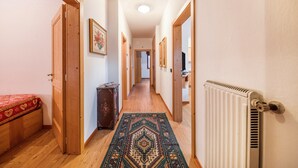 Un couloir étroit avec des portes en bois, un radiateur et un tapis à motifs.