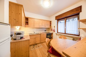 Une cuisine de taille réduite, dotée de meubles en bois, d’une table à manger et d’une fenêtre agrémentée de rideaux.