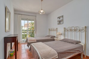 A bedroom with two beds, a desk, a chair, a window with curtains, and a hanging light fixture.
